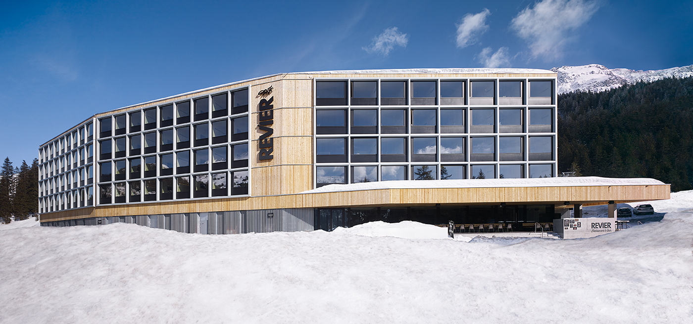 Hotelgebäude mit grosser Glasfassade vor schneebedeckten Bergen